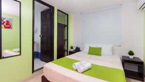 A hotel room with a bed, a bedside table with a phone and a plant, a mirror, and a green wall. - Hotel Avexi Suites By Geh Suites (Cartagena)