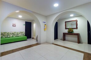 A reception area with a green sofa, a wooden console table with a mirror, and a tiled floor. - Hotel Avexi Suites By Geh Suites (Cartagena)