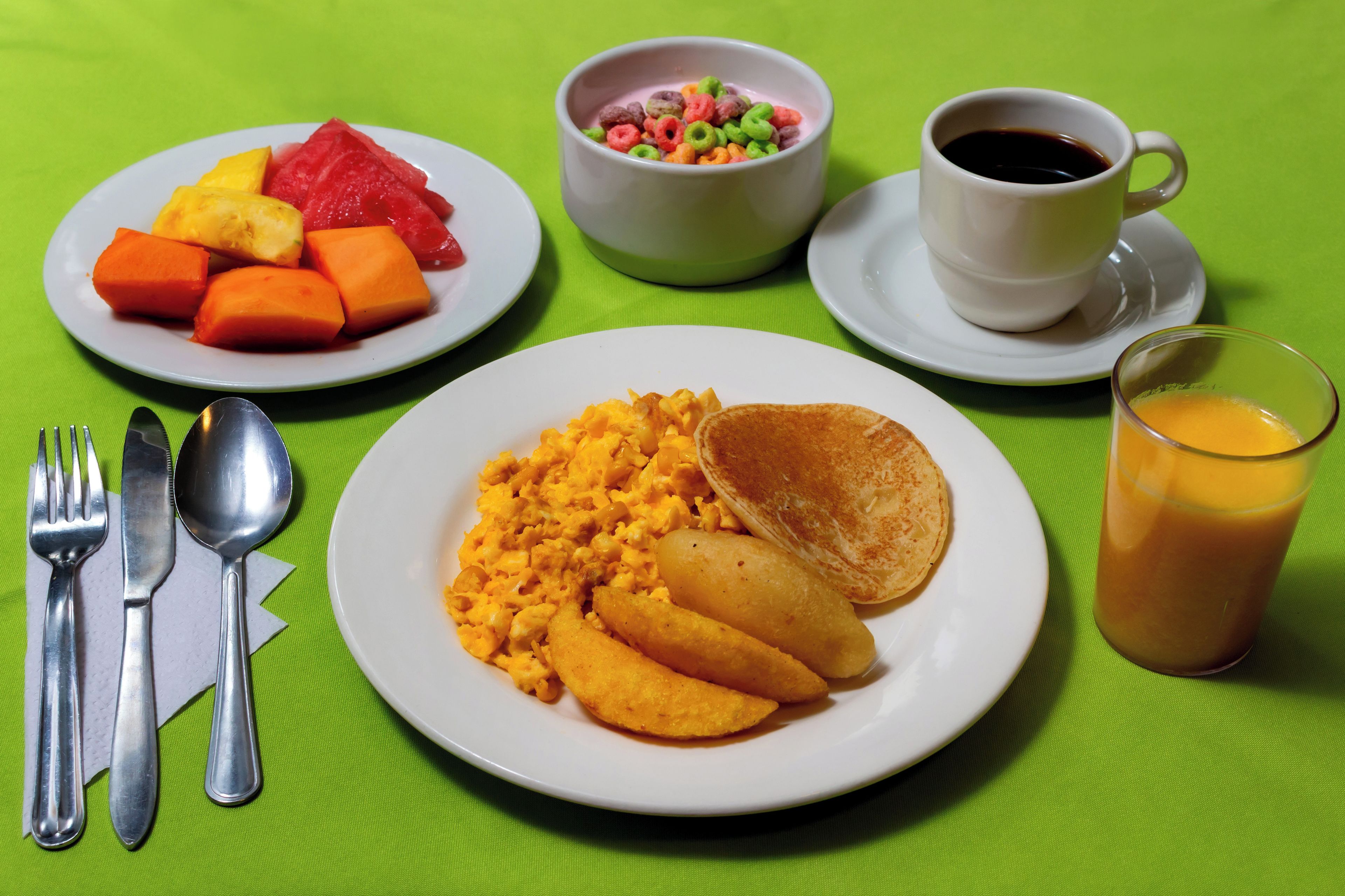 Une table mise pour le petit-déjeuner, avec des assiettes remplies de nourriture, une tasse de café et un verre de jus d’orange.