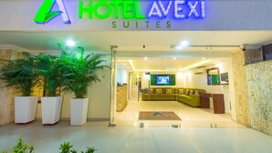 A hotel entrance with a modern sign, a reception area with a sofa, and potted plants. - Hotel Avexi Suites By Geh Suites (Cartagena)