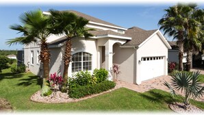 A single-story house with a white exterior, a garage, and a well-maintained front yard with palm trees and shrubs. - 5BR Davenport Pool Home by Watson-465GE (Davenport)