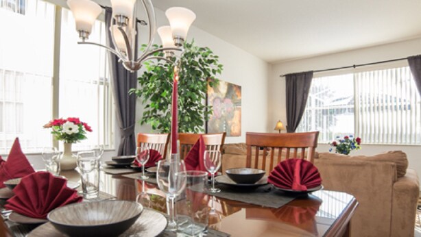 A dining area with a table set for four, a chandelier, and a large window with curtains. - 5BR Davenport Pool Home by Watson-465GE (Davenport)