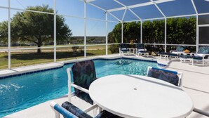 A covered outdoor swimming pool with lounge chairs and a table, surrounded by a white fence and trees. - 5BR Davenport Pool Home by Watson-465GE (Davenport)