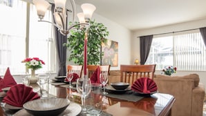 Un coin repas avec une table dressée pour quatre personnes, un lustre et une grande fenêtre agrémentée de rideaux.