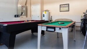 Une table de billard avec des billes, une queue de billard et une table de billard dans une pièce où l’on trouve une porte, un réfrigérateur et un tableau encadré au mur.