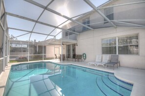 A covered outdoor swimming pool with clear glass panels, a patio area with lounge chairs, and a view of the surrounding landscape.