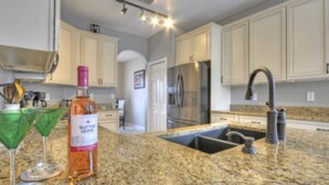 A kitchen with white cabinets, a granite countertop, a stainless steel refrigerator, and a sink with a modern faucet. - 5BR Haines City PoolHome by Watson-186MN (Haines City)