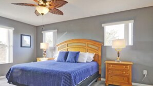A bedroom with a large bed, a wooden headboard, two bedside tables with lamps, and a ceiling fan. - 5BR Haines City PoolHome by Watson-186MN (Haines City)