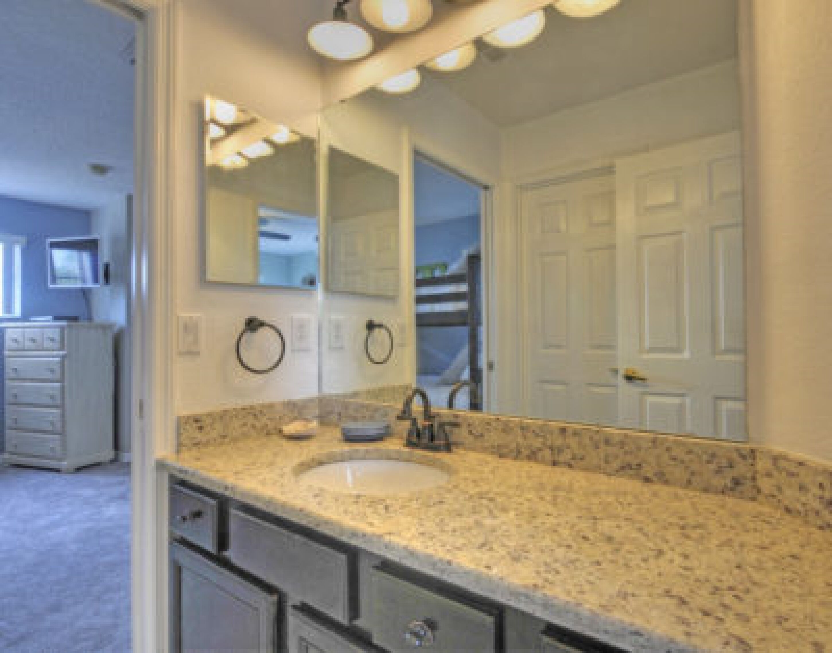 A bathroom with a granite countertop sink, a large mirror, and a white door.
