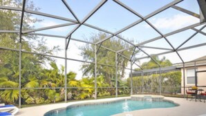 An indoor swimming pool with clear glass walls, surrounded by lounge chairs and a tropical garden view. - 5BR Haines City PoolHome by Watson-186MN (Haines City)