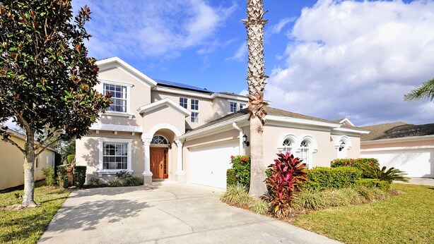A two-story house with a front garage, a driveway, and a well-maintained lawn with a palm tree. - 5BR Haines City PoolHome by Watson-186MN (Haines City)