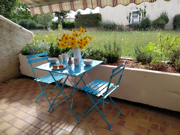 A patio with a blue table and chairs, a white pitcher, and yellow flowers.