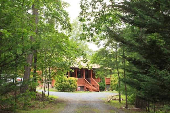 A lodge with a wooden exterior, a gravel driveway, and a staircase leading to the entrance.