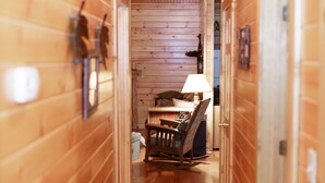 Un estrecho pasillo de madera con una cama, un sillón mecedora y una mesa con una lámpara.