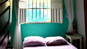 Une pièce avec un lit, une fenêtre avec des rideaux, un ventilateur de plafond et un mur vert.