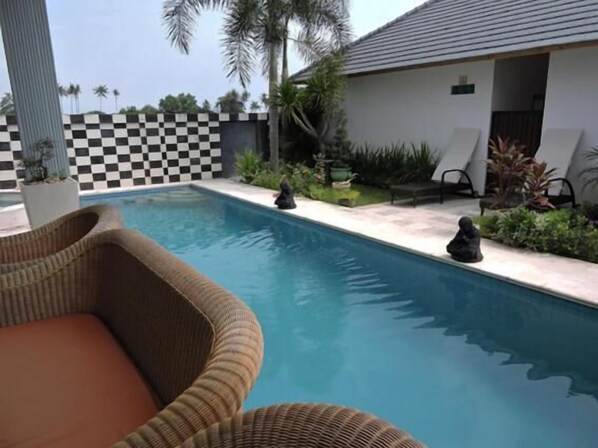 A pool with a checkered wall, lounge chairs, and a small garden area with palm trees. - Kartika Villas (Buleleng)