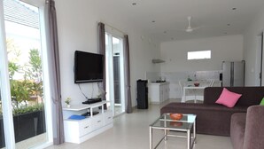 A modern living room with a flat-screen TV, a sofa, a coffee table, and a kitchen in the background. - Kartika Villas (Buleleng)