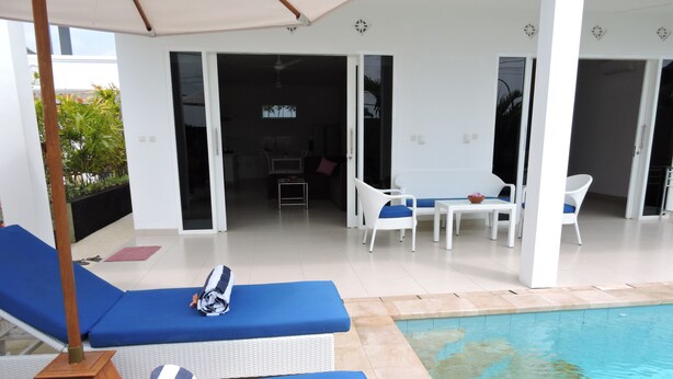 A poolside area with lounge chairs, a table, and a view of the pool. - Kartika Villas (Buleleng)