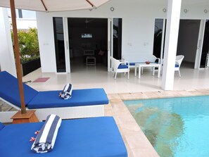 A poolside area with lounge chairs, a table, and a view of the pool. - Kartika Villas (Buleleng)