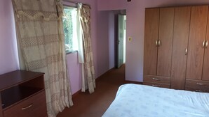 A bedroom with a bed, wooden wardrobe, and a window with curtains. - Beautiful house in Country steps from the Paraná River (Ituzaingo)