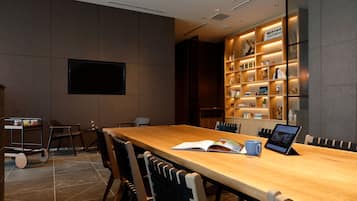 A modern conference room with a long table, chairs, a television, and a bookshelf with various items.