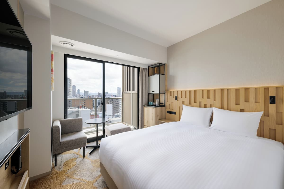 Een hotelkamer met een groot bed, een televisie, een zithoek en uitzicht op de stad.