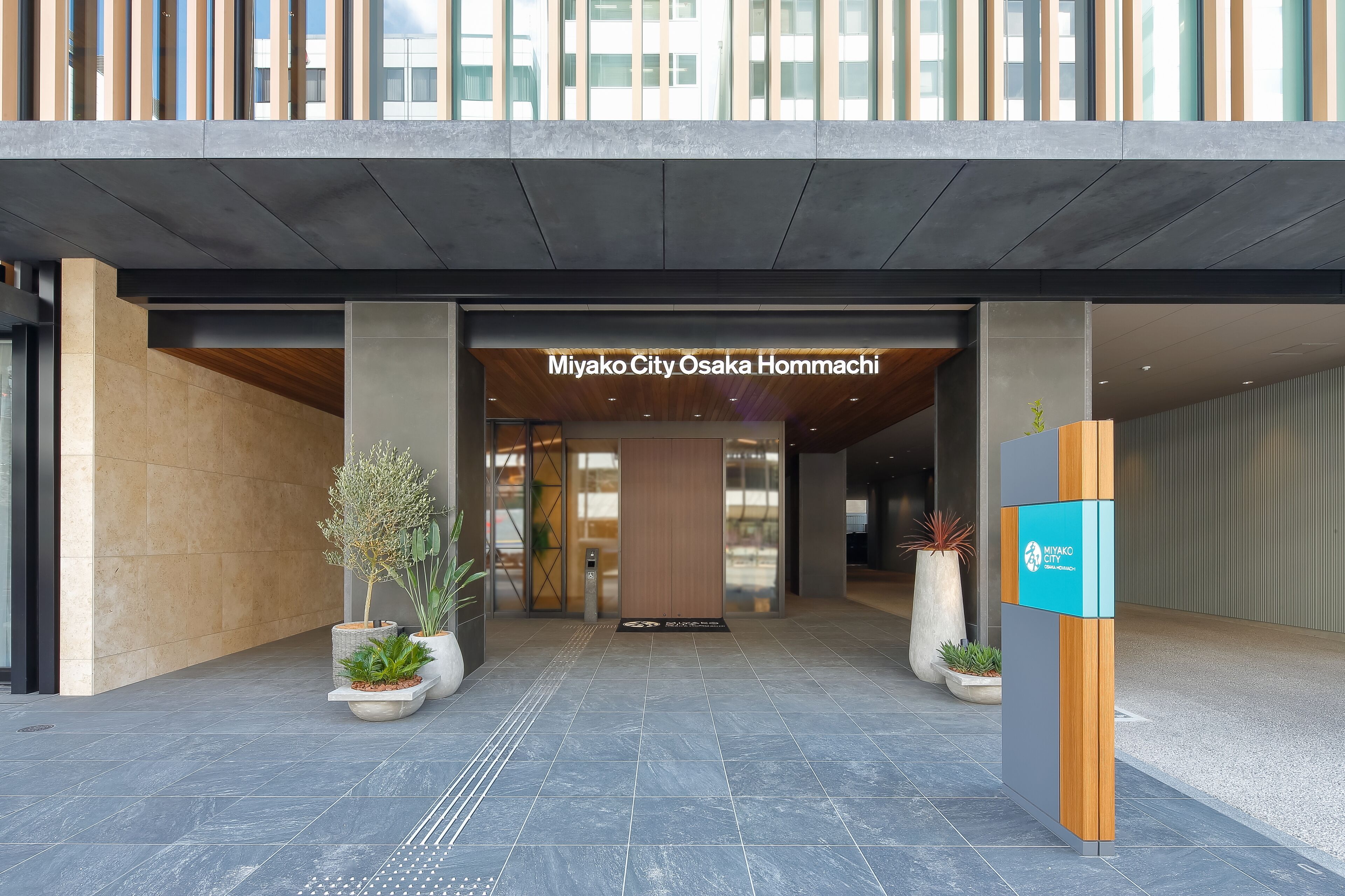 Miyako City Osaka Hommachi -hotellin moderni sisäänkäynti on helposti tunnistettavissa selkeän opastekyltin, ruukkukasvien ja laatoitetun lattian ansiosta.