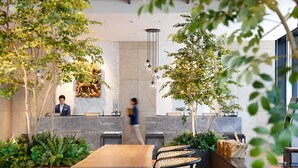 A modern reception area with a marble reception desk, a seating area with a long table and chairs, and indoor plants. - Miyako City Osaka Hommachi (Osaka)