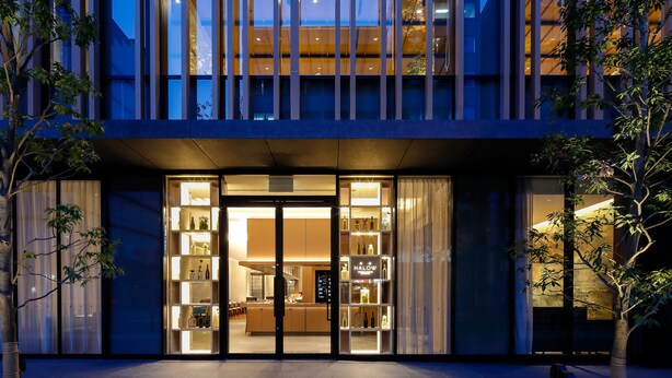 A modern building with a glass facade, a well-lit entrance, and a visible interior with shelves and a counter. - Miyako City Osaka Hommachi (Osaka)