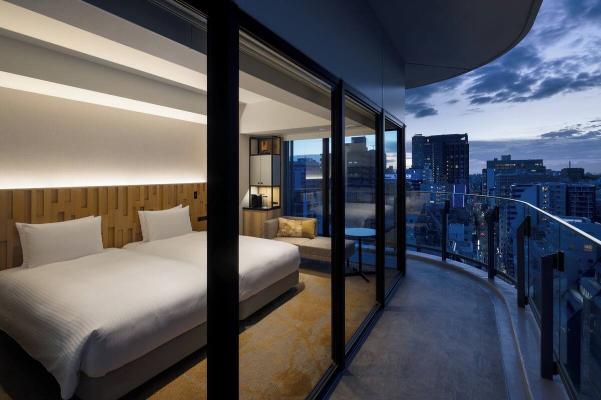Een moderne hotelkamer met een groot bed, een zithoek en een balkon met uitzicht op de stad.