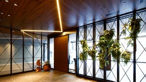 A modern interior with wooden ceiling panels, large windows with black frames, and hanging plants. - Miyako City Osaka Hommachi (Osaka)