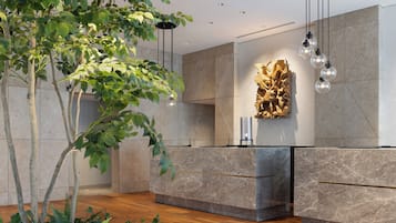 A modern reception area with a marble reception desk, hanging pendant lights, and a wall-mounted sculpture.