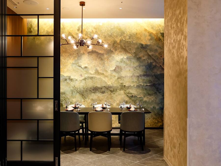 A dining area with a marble wall, a chandelier, and a table set for four.