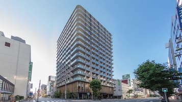 A modern high-rise building with multiple balconies, located at a city intersection.