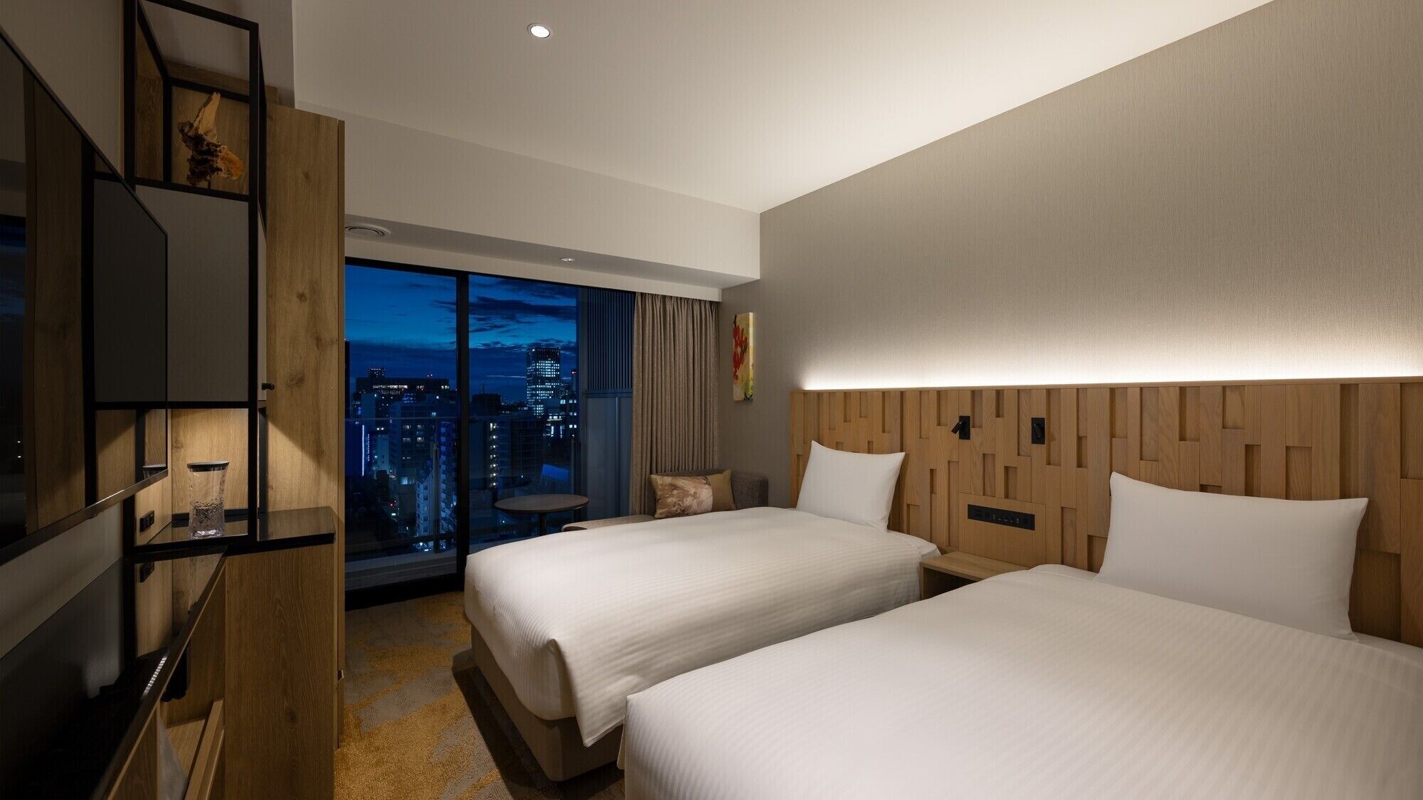 A hotel room with two beds, a TV, a city view, and a wooden headboard.