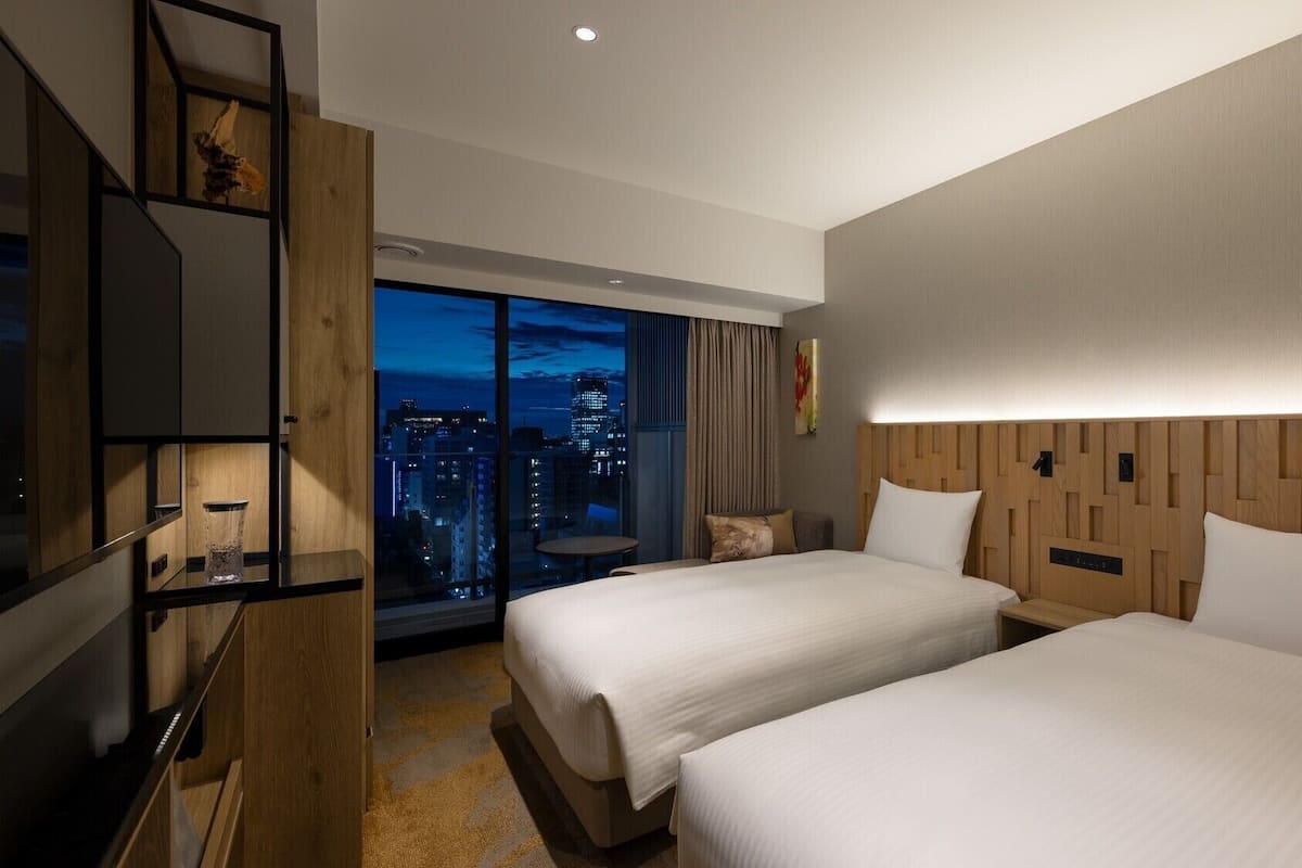 Een hotelkamer met twee bedden, een televisie, uitzicht op de stad en een houten hoofdeinde.