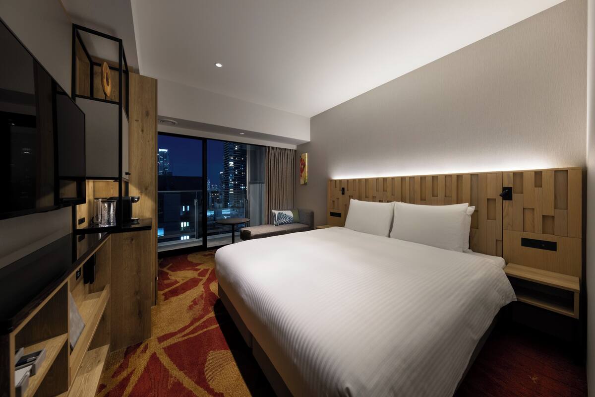 Een moderne hotelkamer met een groot bed, een televisie, een houten hoofdeinde en uitzicht op de stad.