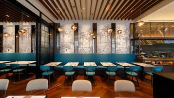 A restaurant with wooden ceiling slats, blue cushioned booths, and hanging pendant lights.