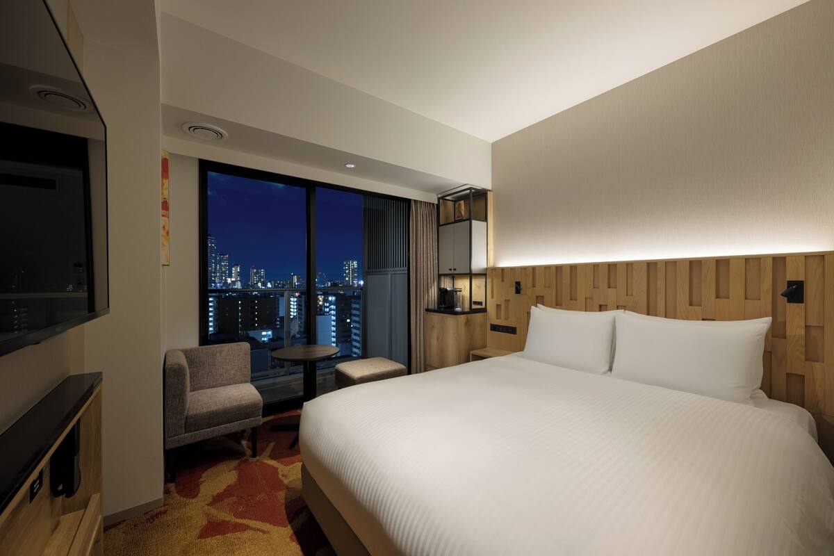 Hotelkamer met een groot bed, een televisie, een zithoek met uitzicht op de stad en een houten hoofdeinde.