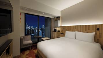 Une chambre d’hôtel dotée d’un grand lit, d’une télévision, d’un coin salon avec vue sur le paysage urbain et d’une tête de lit en bois.