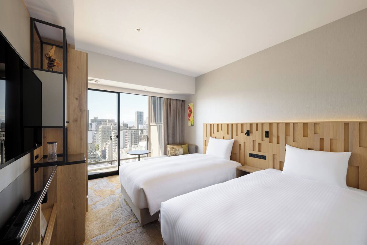 Een hotelkamer met twee bedden, een groot raam met uitzicht op de stad, een houten hoofdbord en een flatscreen televisie.