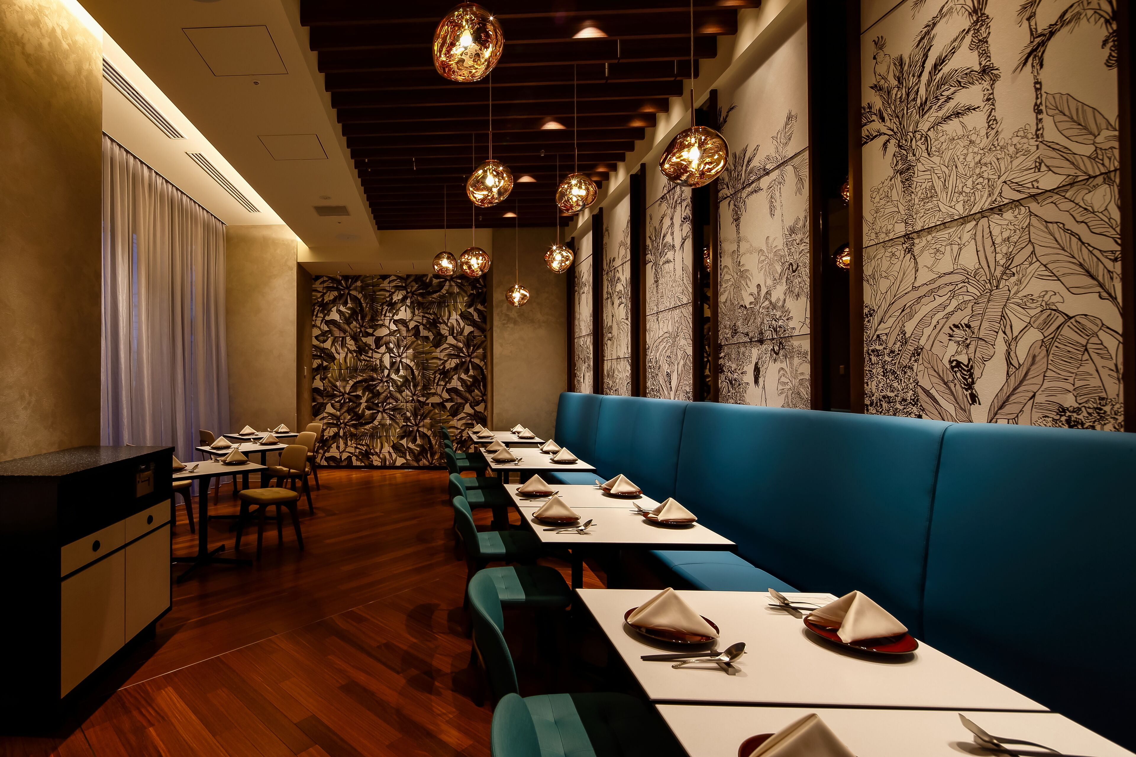 A restaurant with long tables, blue booths, and hanging spherical lights.