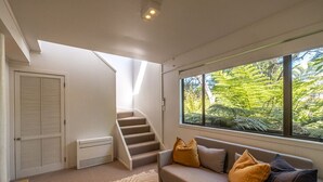 Una sala de estar moderna con una escalera, un ventanal con vistas a la vegetación y un sofá color beige con cojines.