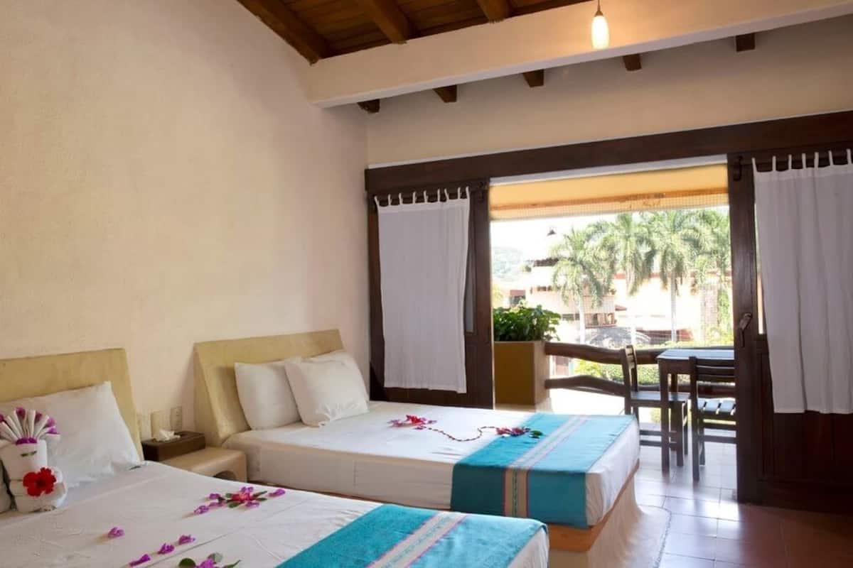 Habitación de hotel con dos camas, techo de madera y vistas a palmeras.