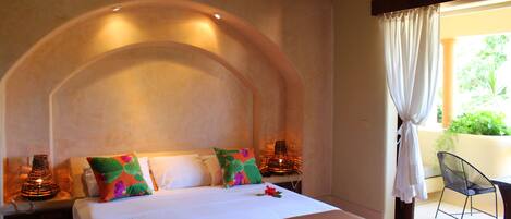 A hotel room with a large bed, a curved ceiling, and a view of greenery outside.