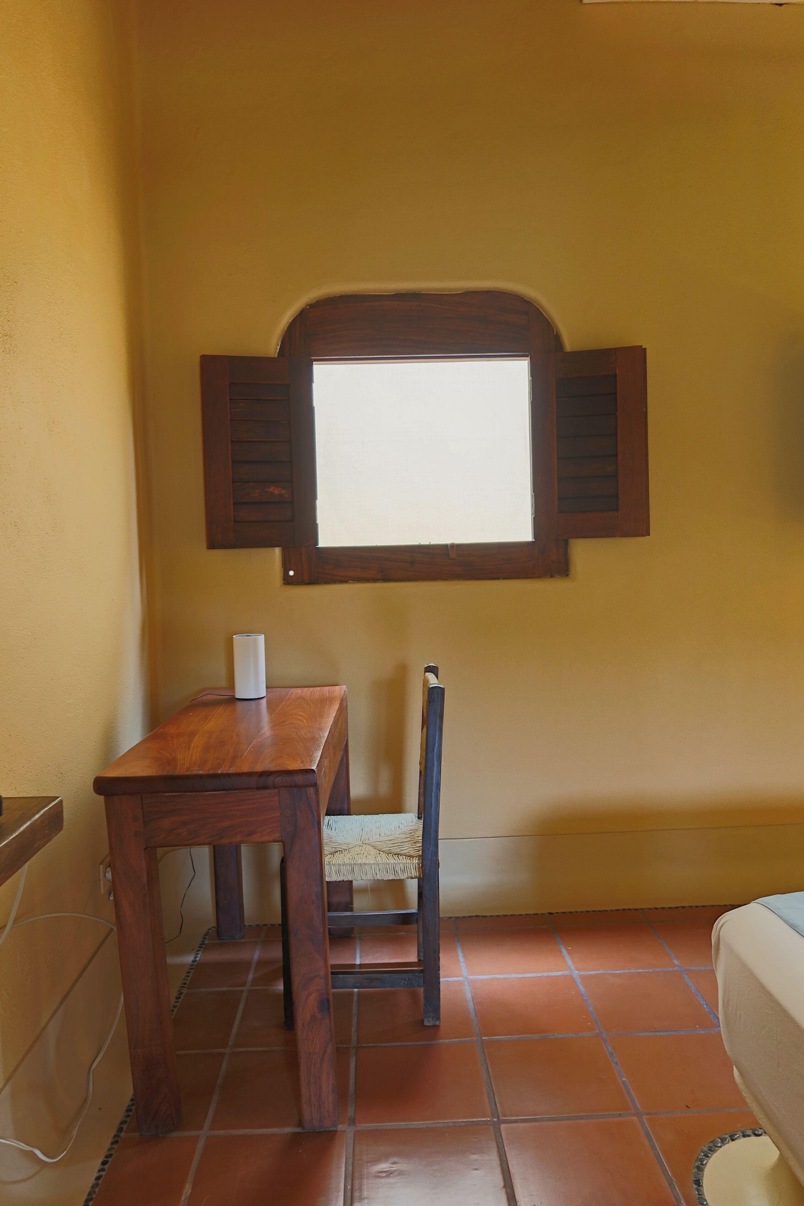 A room with a wooden table, a chair, a window with shutters, and a tiled floor.