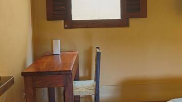 A room with a wooden table, a chair, a window with shutters, and a tiled floor.
