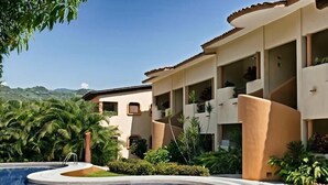 A resort with a swimming pool, palm trees, and a mountainous backdrop.