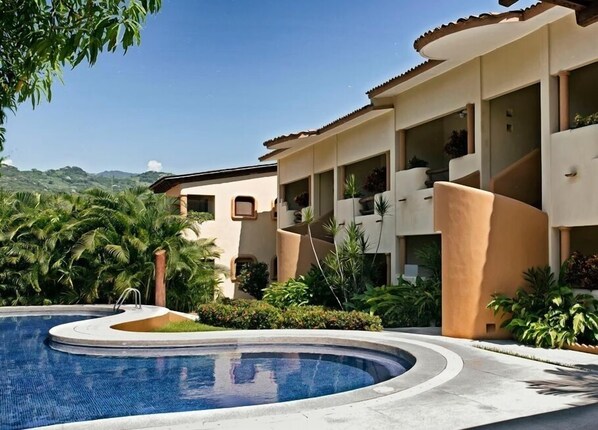A resort with a swimming pool, palm trees, and a mountainous backdrop.