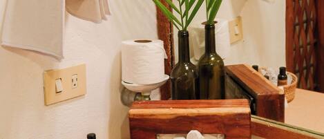 Een badkamer met een houten wastafelmeubel, een spiegel, een wastafel, een handdoekhouder, een plant en een mandje met toiletartikelen.